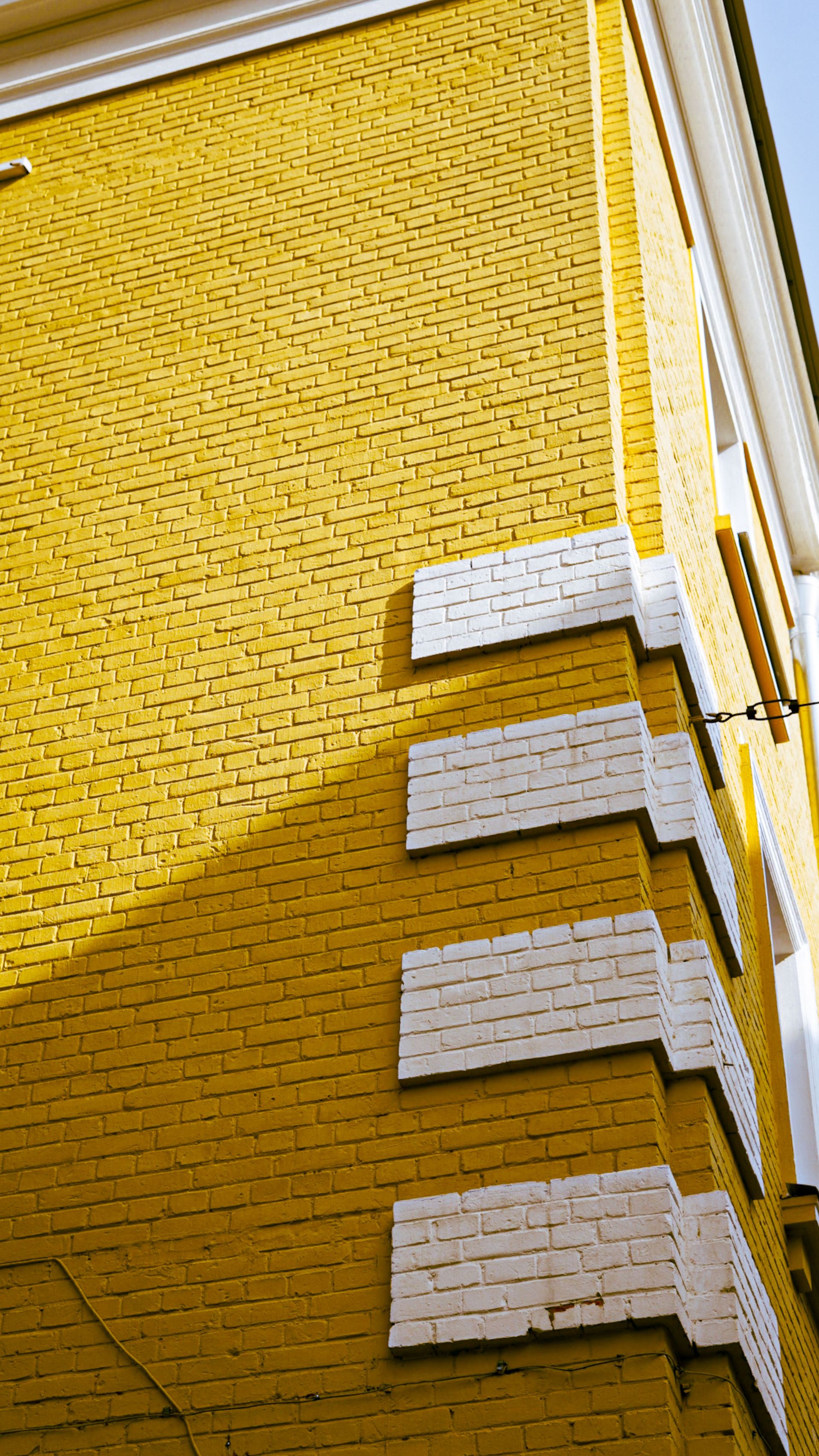 Vertical view of a striking yellow brick building corner featuring contrasting white accents and dramatic shadows.